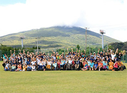 100名を超える多様な参加者が集まったユニバーサルキャンプin八丈島。山を背景にしたユニバーサルキャンプ参加者の集合写