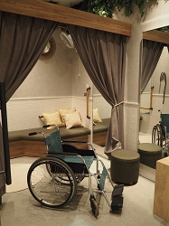 画像　フィッティングルームの出入口に車椅子が置いてあり、車椅子でも出入りできる広さであることが分かる写真